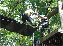 A challenge course participant is assisted by staff over a high ropes element